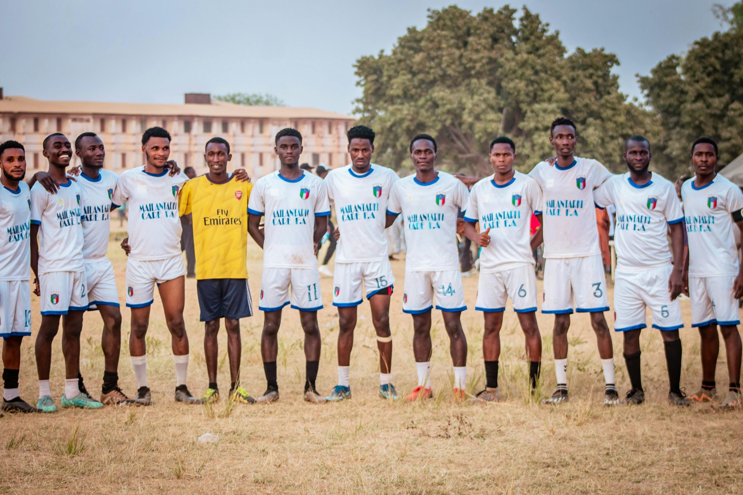A diverse soccer team poses together outdoors on a field in a group photo.